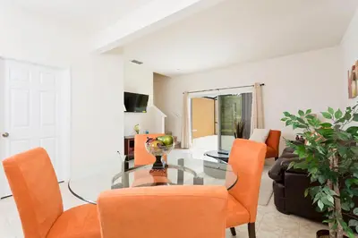 a living room with a glass table and orange chairs at 3Br 3Bath Townhome BBQ Pool 15min Disney 1291ft in Kissimmee