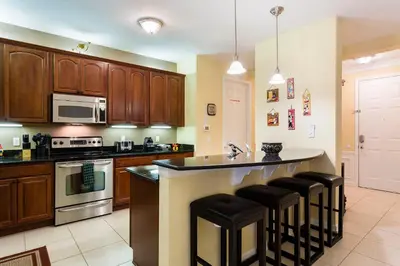 a kitchen with wooden cabinets and a island with bar stools at 4Br 2Bath Condo Balcony 5min Conv Center 2020ft in Orlando