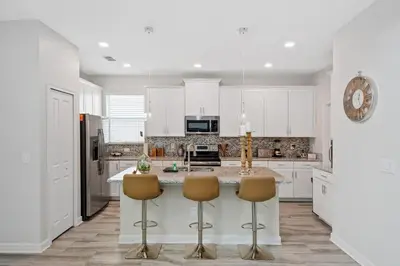 a kitchen with white cabinets and a kitchen island with chairs at 5Br 5Bath Pvt Home BBQ Pool 10min Disney 3077ft in Kissimmee