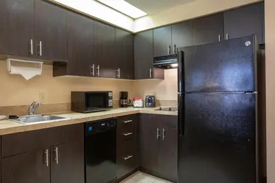 a kitchen with wooden cabinets and a black refrigerator at staySky Suites I-Drive Orlando Near Universal in Orlando