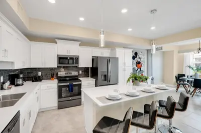 a kitchen with white cabinets and a kitchen island with chairs at NEW Magically Themed Condo w Pool View in Kissimmee