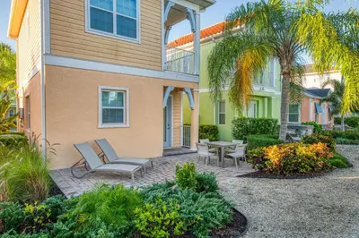 a patio with chairs and tables in front of a house at Cozy Peach Cottage Near Disney With Margaritaville Resort & Island H2O Access - 8029Dr in Orlando