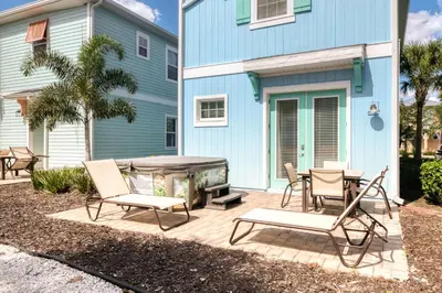 a patio with chairs and a fire pit in front of a blue house at Vibrant Cottage With Hot Tub Near Disney With Margaritaville Resort & Island H2O Access - 8032Dr in Orlando
