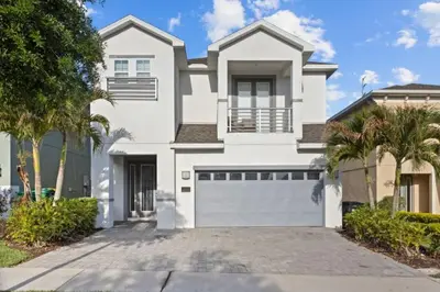 a white house with a garage and palm trees at 360 Pendant Ct · 360 Villa - 7BD - Pool Theme Beds by Disney in Orlando
