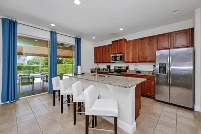 a kitchen with wooden cabinets and a bar with white chairs at Luxury Home With Private Pool And Water Park & Resort Access Near Disney At Encore Resorts Reunion - 240Mn in Kissimmee