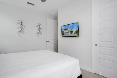 a white bedroom with a bed and a tv on the wall at Stylish Family Home Private Pool/Spa 10min Disneyworld Sleeps 22 in Orlando
