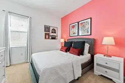 a bedroom with a pink wall and a bed with red pillows at Fresh Amazing Family Home. Private Pool. Game Room. Sleeps 24 in Kissimmee