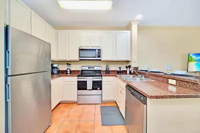 a kitchen with white cabinets and a stainless steel refrigerator at Near Disney - Spacious 3BR Condo with Pool in Orlando
