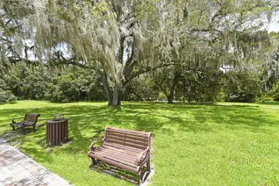 a park bench sitting in the grass under a tree at Lakeside 4-Bed Pool Home at Villa Sol home in Kissimmee