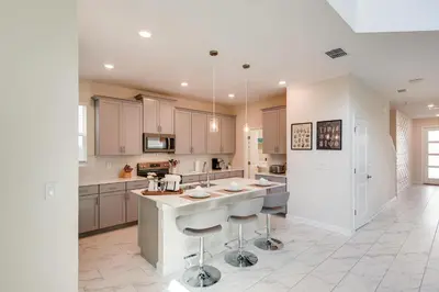 a large kitchen with white cabinets and a island with bar stools at 2751 BD -Luxury 5BR Single Family - Private Pool in Kissimmee