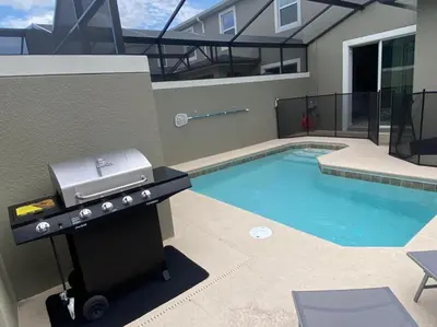 a barbecue grill next to a building with a swimming pool at 4321 QS - Magical Haven Townhome w Pool in Kissimmee