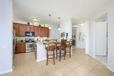 an open kitchen with wooden cabinets and bar stools at Epic Universe Vista Cay Lakeview Condo - 1019 in Orlando