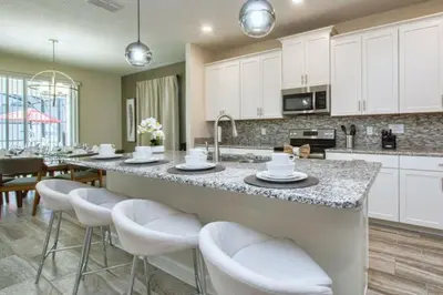 a kitchen with white cabinets and a bar with stools at 4712 Fabulous Brand-New Private Pool in Kissimmee