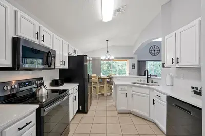 a kitchen with white cabinets and a black refrigerator at Walkin' on Sunshine - 5 bed pool home in Terra Verde Resort near Disney in Kissimmee