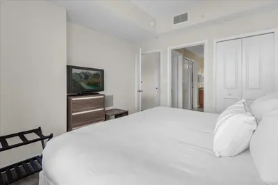 a white bedroom with a bed and a television at The Point, Lux Apartment 4 min from Universal in Orlando