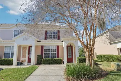 a white house with a red door and a tree at Veteran Owned 3bdr/3 bath Townhouse w/WiFi 3mi to Disney - Winter/Spring Specials in Kissimmee