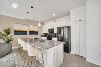 a kitchen with white cabinets and a kitchen island with bar stools at Amazing Story Lake Town Home With Pool townhouse in Kissimmee