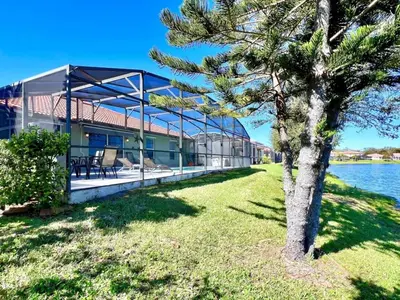 a house on the water with a tree in the foreground at Lovely Lakeside 4-Bed Pool Home at Villa Sol-3125 home in Kissimmee