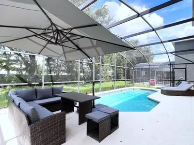 a patio with a couch and an umbrella next to a pool at Spacious 7Bd Pool Gm Hm Terra Verde Resort-211HBL home in Kissimmee