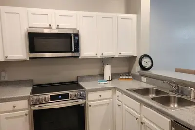 a kitchen with white cabinets and a microwave and a sink at Apartment Kissimmee - Orlando in Kissimmee