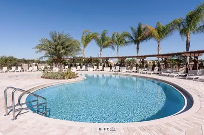 a pool with chairs and palm trees in a resort at Lovely and Cozy Townhome Near Disney Parks in Kissimmee