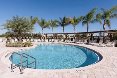 a pool with chairs and palm trees in a resort at Lovely and Cozy Townhome Near Disney Parks in Kissimmee