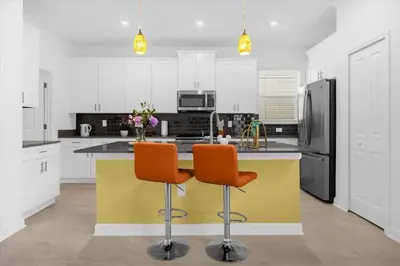 a kitchen with a yellow island with two orange chairs at Stylish Resort Villa w Pool Near Disney Gated 5BR in Kissimmee