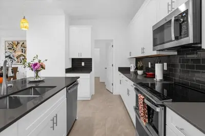 a kitchen with white cabinets and black counter tops at Stylish Resort Villa w Pool Near Disney Gated 5BR in Kissimmee