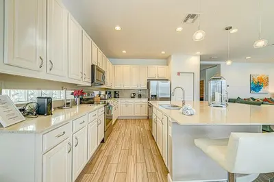 a large kitchen with white cabinets and wooden floors at #371-Stunning 6 bed with modern decor, south facing pool and spa overlooking water in Kissimmee