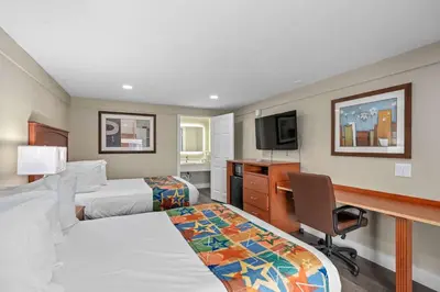 a hotel room with two beds and a desk at Travelodge by Wyndham Kissimmee Orlando in Kissimmee