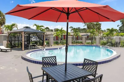 a table with a red umbrella next to a swimming pool at Travelodge by Wyndham Kissimmee Orlando in Kissimmee