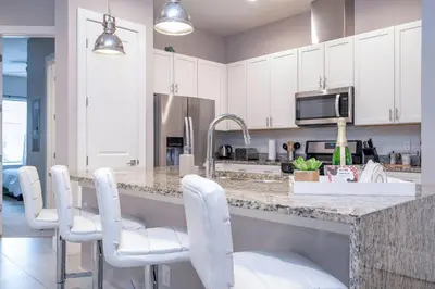 a kitchen with white cabinets and a counter with white chairs at Gorgeous NEW 4 Beds Dream Villa 5 min to Disney in Orlando